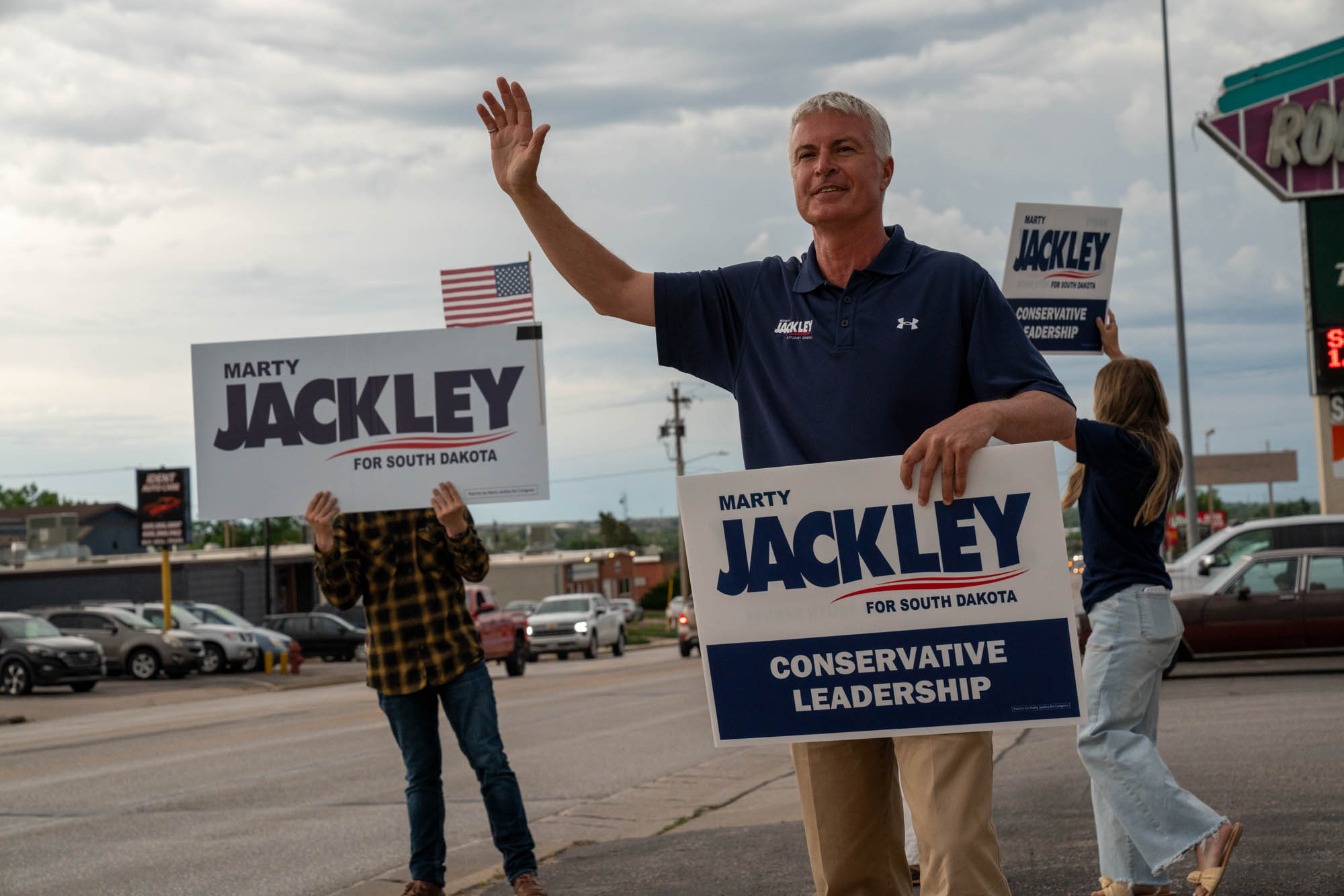 Marty Jackley waves to passing cars with supporters and campaign signs